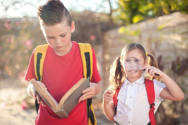 Alunos com livro e lupa ao ar livre. De volta à escola. Crianças e conceito de educação