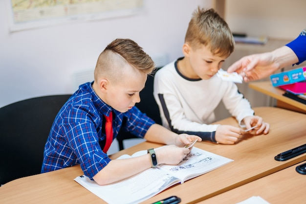 Alunos concentrados sentados na mesa e escrevendo no livro de exercícios com o colega sentado atrás.