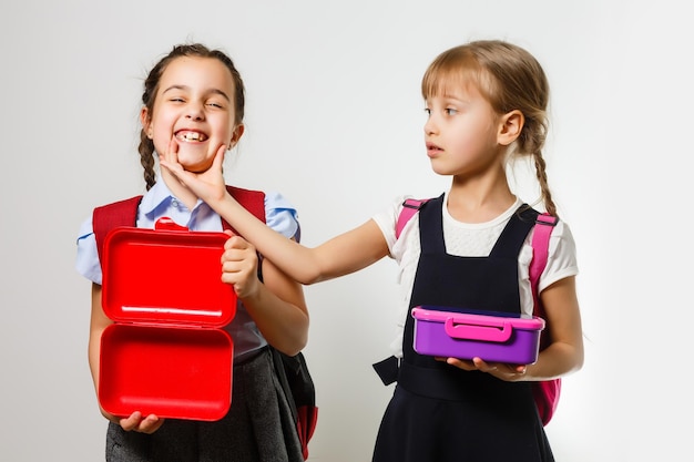 Foto alunos da escola primária com lancheiras nas mãos. meninas com mochilas estão comendo frutas. início das aulas. primeiro dia de outono.