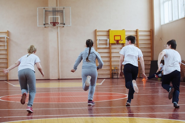 Alunos da escola primária uma aula de esporte dentro de casa. As crianças correm e jogam jogos móveis.