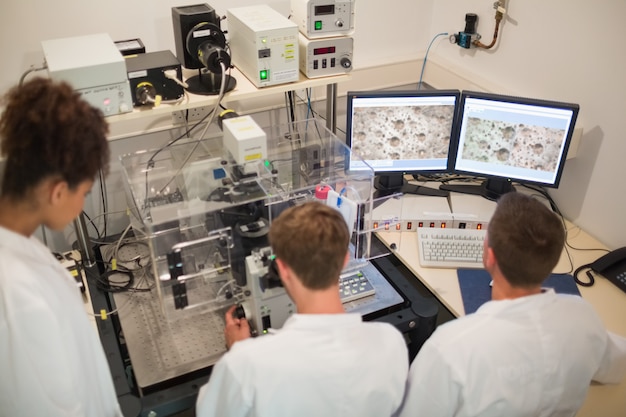 Alunos de bioquímica usando microscópio grande e computador na universidade
