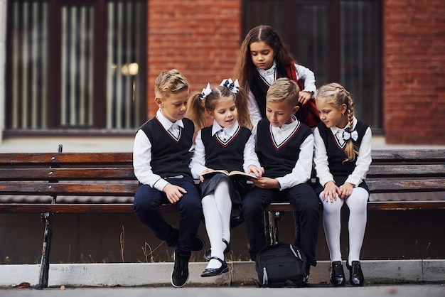 Alunos em uniforme que fica ao ar livre no banco com o bloco de notas.