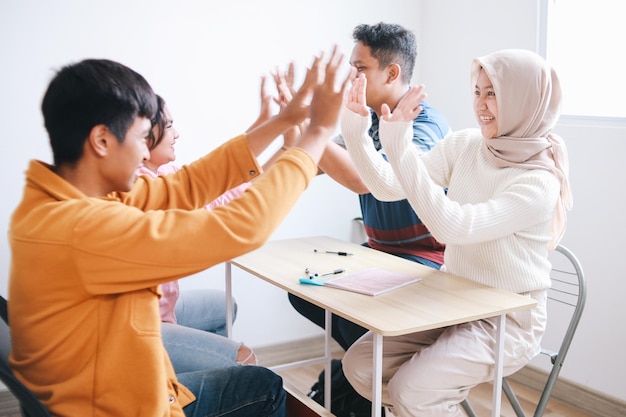 Alunos entusiasmados comemorando conquistas e trabalho em equipe dando um "high five" juntos na sala de aula