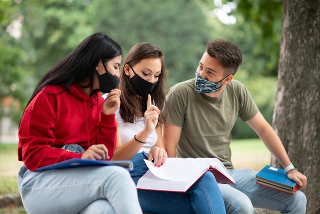 Alunos estudando juntos sentados em um banco ao ar livre e usando máscaras covid