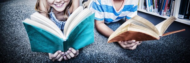 Foto alunos felizes deitados no chão e lendo um livro na biblioteca