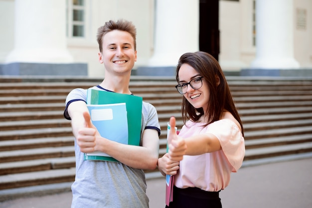 Alunos felizes mostrando o polegar para fora do campus universitário