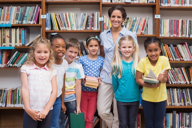 Alunos fofos e professor olhando a câmera na biblioteca