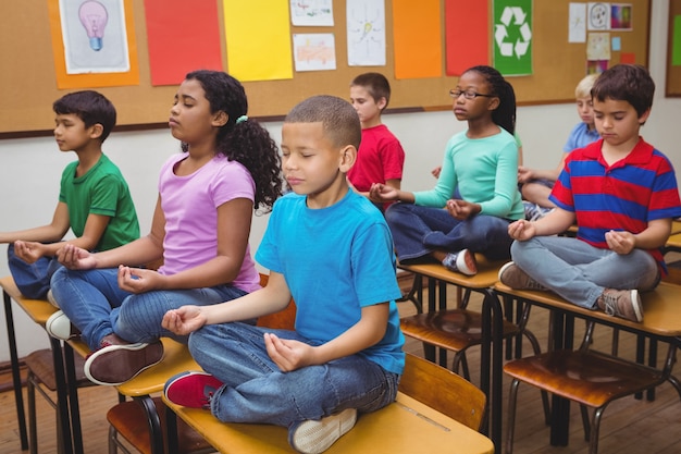 Alunos meditando em mesas de aula