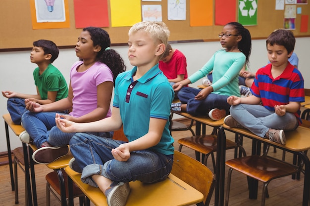 Alunos meditando em mesas de sala de aula