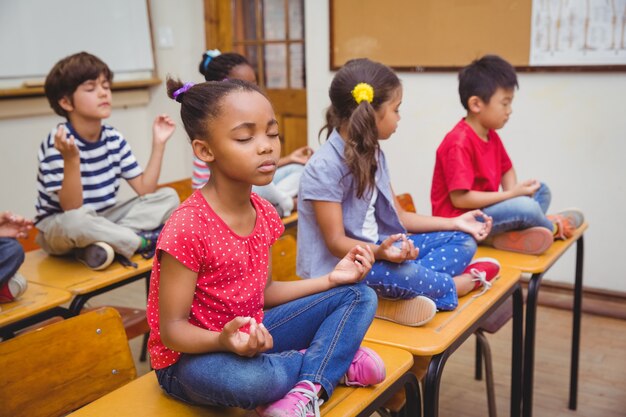 Alunos meditando na posição de lótus na mesa na sala de aula