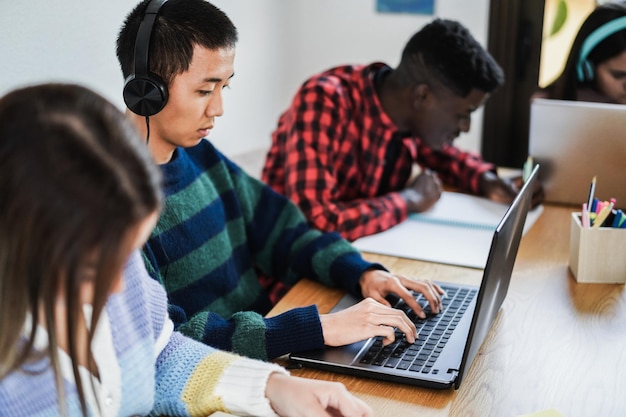 Alunos multirraciais usando laptops enquanto estudam juntos na biblioteca - foco na mão direita asiática