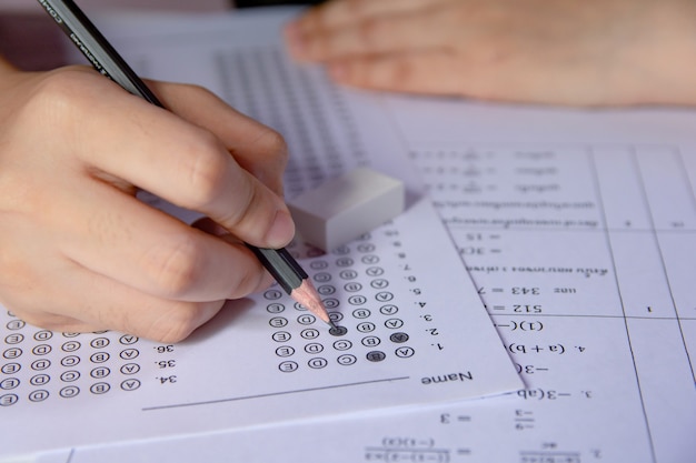 Foto alunos segurando a mão segurando a escrita a lápis, escolha selecionada nas folhas de respostas e folhas de perguntas de matemática. alunos testando fazendo exame. exame escolar