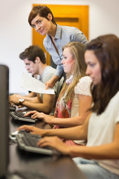 Alunos sentado no computador com o professor olhando