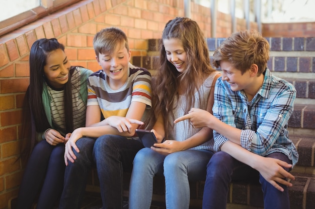 Alunos sorridentes sentados na escada usando um telefone celular