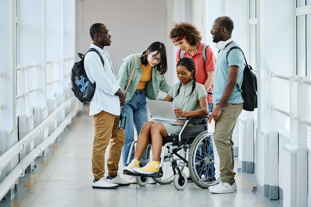 Alunos usando laptop em pé no corredor