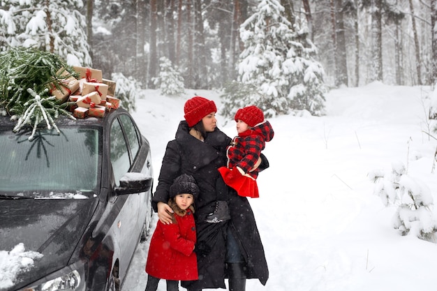 Am Auto steht eine Familie mit Weihnachtsbaum und Geschenken