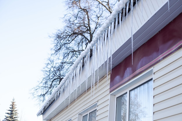 Am Dach des Gebäudes hängen viele Eiszapfen unterschiedlicher Länge. Seitenansicht