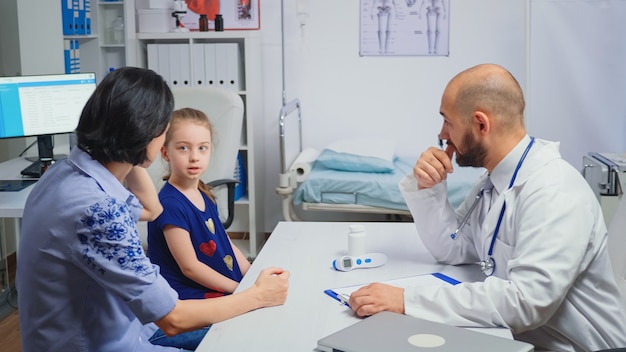 Am Schreibtisch sitzen und Behandlung für krankes Kind schreiben. Heilpraktiker Arzt Facharzt für Medizin, der Gesundheitsdienste erbringt Röntgenuntersuchung im Krankenhausschrank