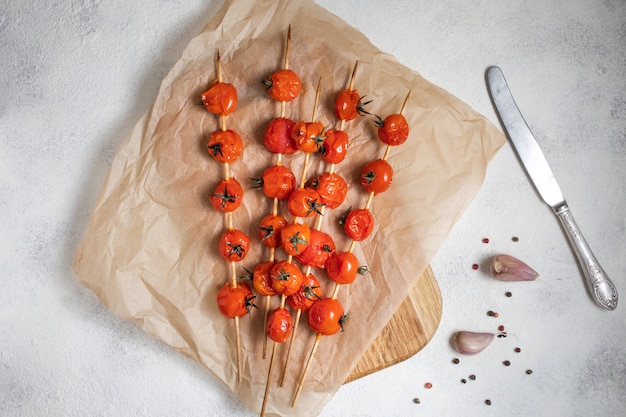 Am Spieß gegrillte Kirschtomaten auf Backpapier legen. Mit Olivenöl, Knoblauch, Salz und Pfeffer gekocht