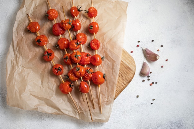 Am Spieß gegrillte Kirschtomaten auf Backpapier legen. Mit Olivenöl, Knoblauch, Salz und Pfeffer gekocht