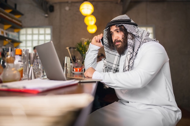 Am Telefon arabischer Geschäftsmann, der im Büro-Business-Center mit Geräte-Gadget arbeitet