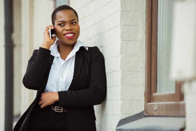 Am Telefon sprechen Afroamerikanische Geschäftsfrau in Bürokleidung lächelnd sieht selbstbewusst aus
