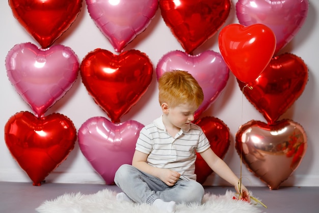 Am Valentinstag, dem 14. Februar, sitzt ein rothaariger Junge zwischen Bällen mit Herzen