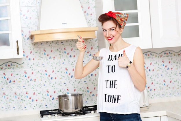 Ama de casa alegre en un pañuelo rojo en la cocina