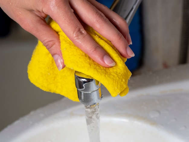 Ama de casa amarillo un paño húmedo para limpiar el grifo del baño. Concepto de limpieza del hogar y mantenimiento de la limpieza.