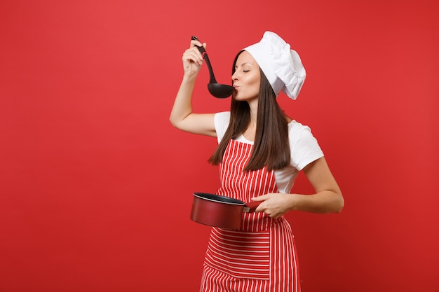 Ama de casa cocinera cocinera o panadero en delantal de rayas camiseta blanca gorro de chef de toque aislado sobre fondo de pared roja. Mujer mantenga degustación cazo de cazo de sopa negra cacerola vacía. Simulacros de concepto de espacio de copia