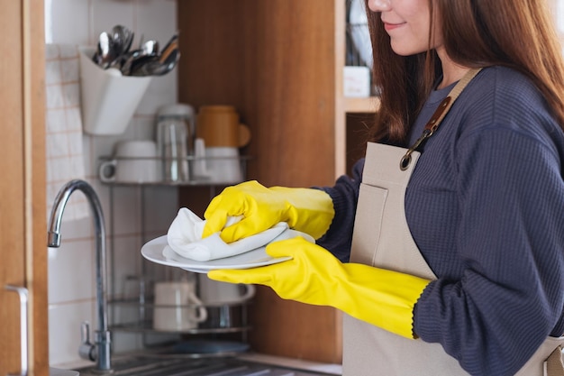 Un ama de casa con delantal y guantes protectores limpiando y lavando platos en la cocina de casa