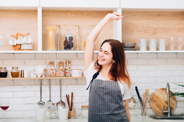 Ama de casa feliz. Cocinando diversión y placer. Mujer joven vistiendo delantal bailando en la cocina.