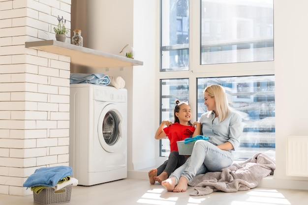 Ama de casa feliz y su hija con sábanas cerca de lavadora