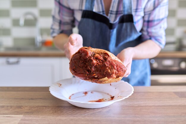 Ama de casa femenina en delantal cocinando carne en casa en la cocina, mujer con carne de cerdo adobada especias pierna cruda