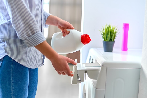 Ama de casa femenina vertiendo gel suavizante de telas en una moderna lavadora