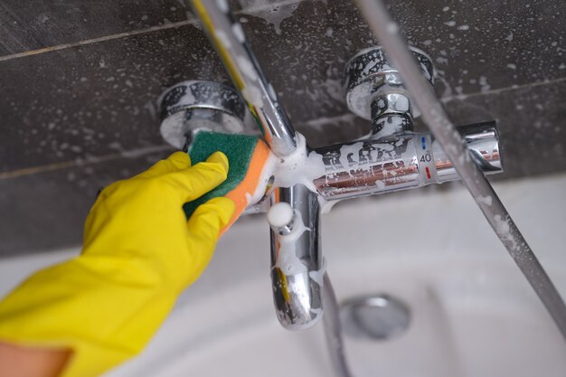 Ama de casa en el grifo de lavado de guantes de goma en el baño con esponja closeup