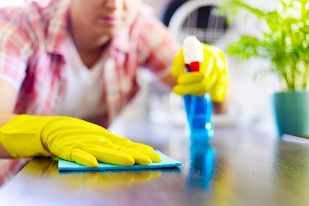 La ama de casa con guantes amarillos limpia el polvo con detergente en aerosol y trapo