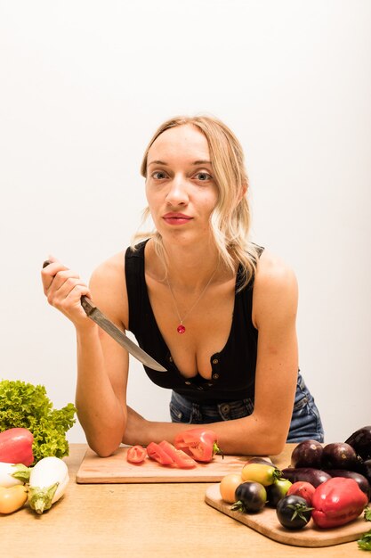 Ama de casa hermosa joven está ocupada preparando comida sana en casa en la cocina