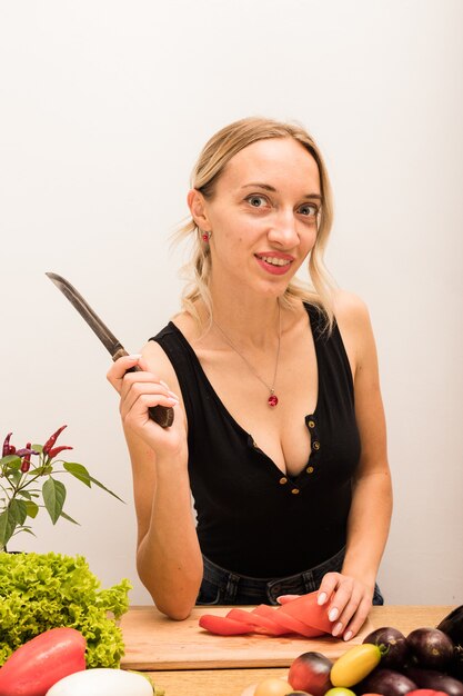 Ama de casa hermosa joven está ocupada preparando comida sana en casa en la cocina