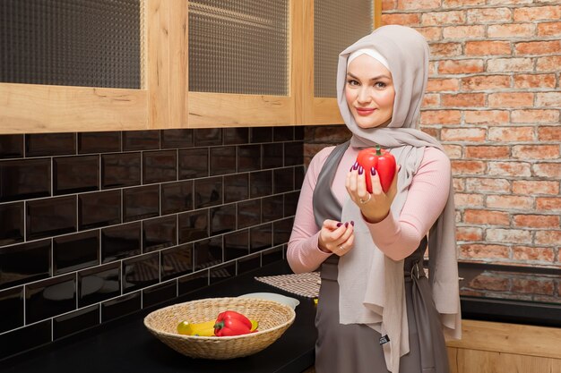 Ama de casa en hijab sostiene y muestra pimienta en mano en la cocina