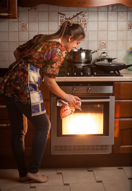 Foto ama de casa joven control de plato de cocción en el horno