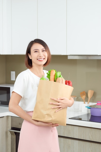 Ama de casa joven feliz con bolsa de compras llena de verduras