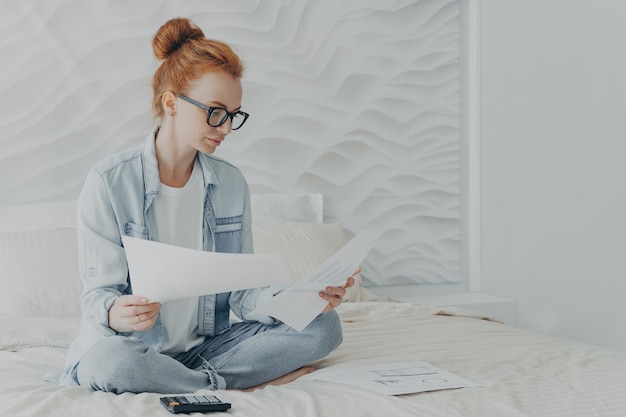 Ama de casa joven mujer concentrada en espectáculos administrar el presupuesto familiar mientras está sentado en la cama en casa