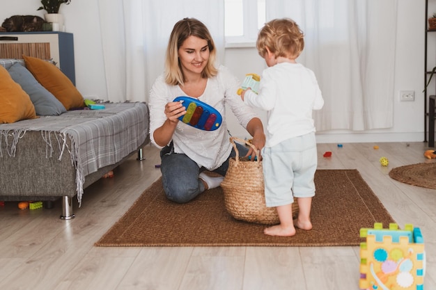 Ama de casa joven pone juguetes en la cesta con su pequeño hijo en casa