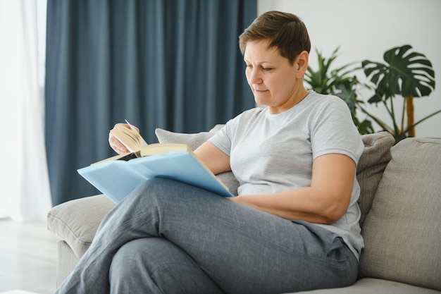 Ama de casa de mediana edad sentada en un sofá con un pasatiempo de retiro de tiempo libre de libros