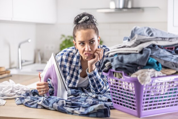 El ama de casa mira a regañadientes la pila de ropa que necesita planchar con una plancha en la mano