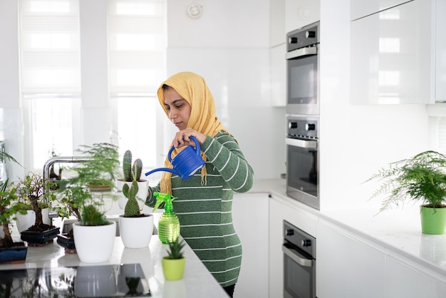 Ama de casa musulmana en casa regando las plantas en la cocina