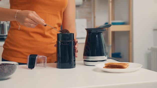 Ama de casa poniendo café en una olla eléctrica durante el desayuno. Ama de casa en casa haciendo café recién molido en la cocina para desayunar, beber, moler café espresso antes de ir a trabajar