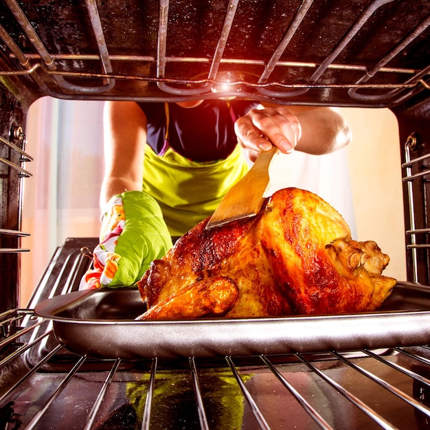 Ama de casa prepara pollo asado en el horno, vista desde el interior del horno. Cocinar en el horno.