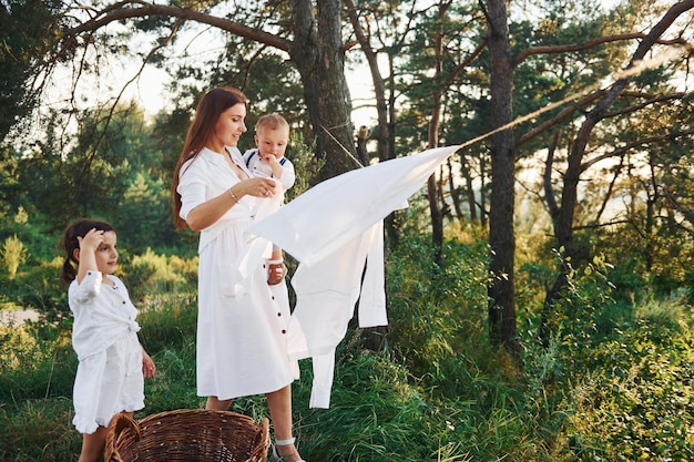 Ama de casa secando ropa Joven madre con su pequeña hija y su hijo está al aire libre en el bosque Hermoso sol